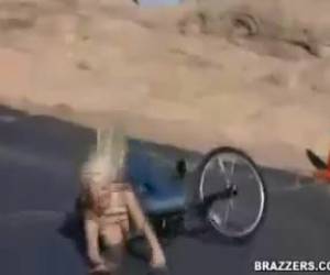 Een blond meisje zit op de fiets. Met haar tieten ontbloot doet ze een faceplant.